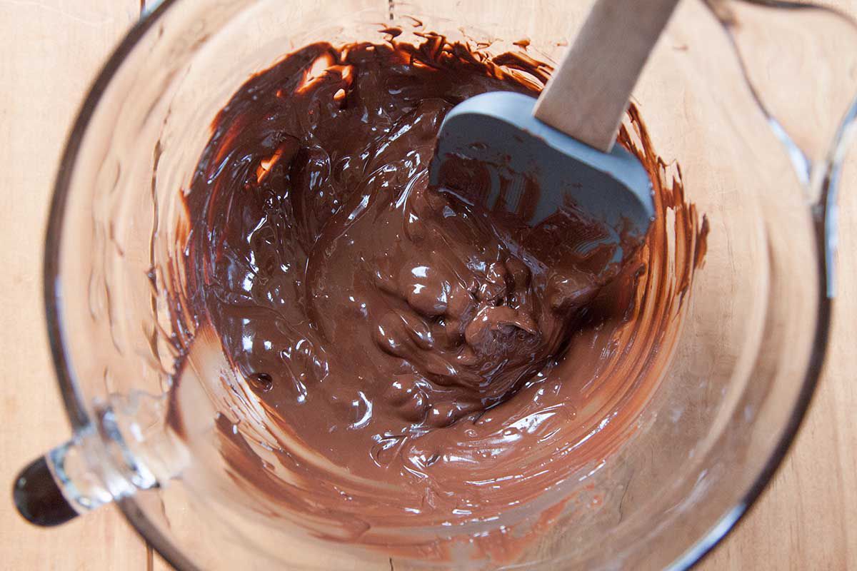 Melted chocolate being stirred in a glass dish with a spatula