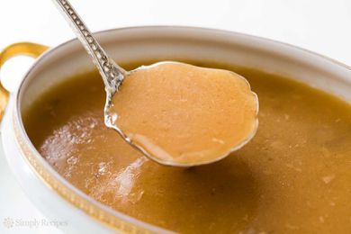 A white gravy boat full of gravy with a spoonful being taken out 