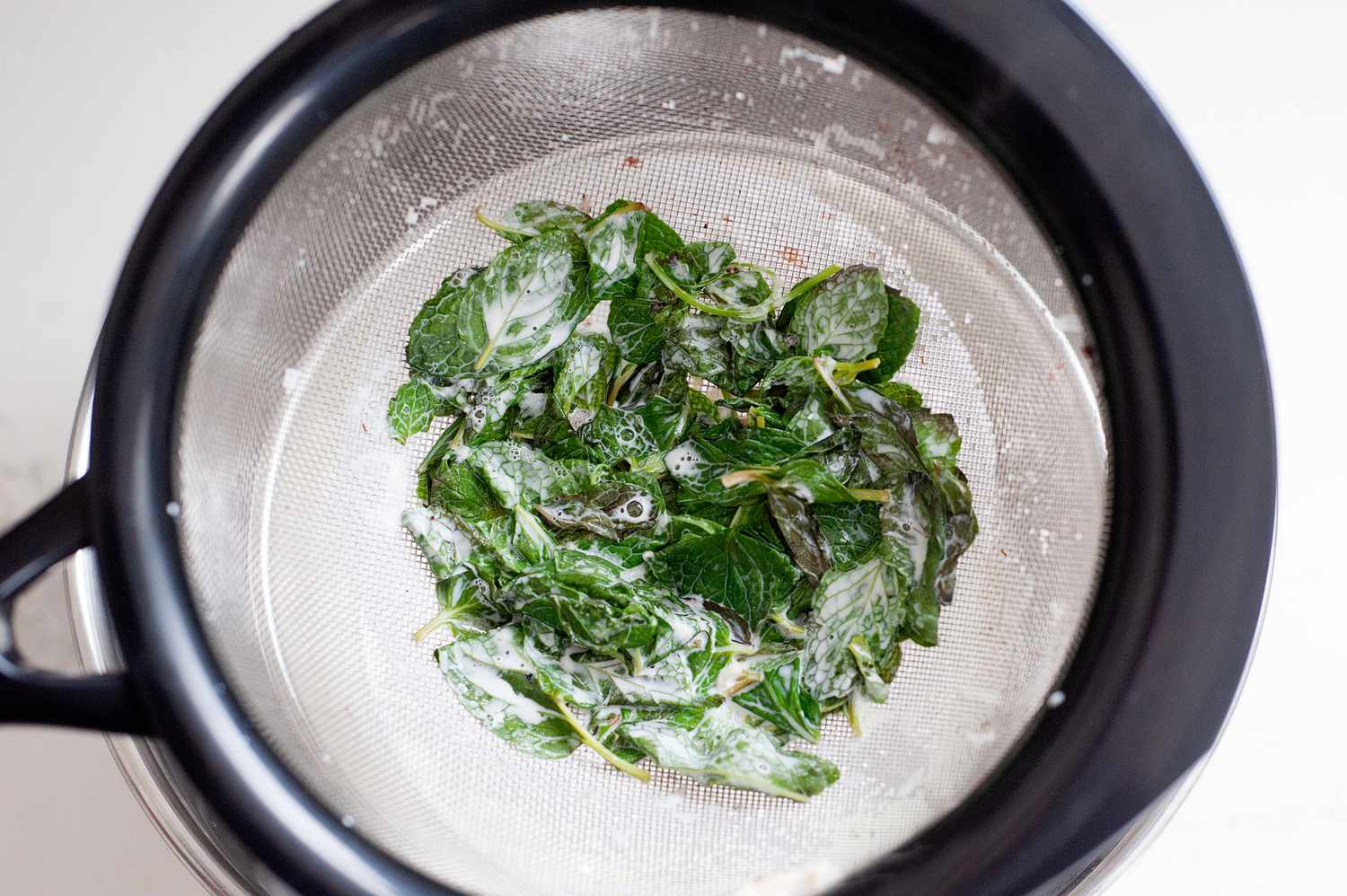 Straining mint chocolate chip base over a water bath.
