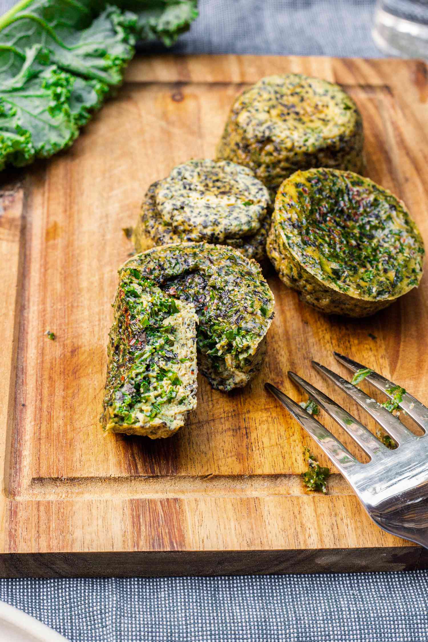 Kale and Portobello Egg Bites on a Cutting Board with One Egg Bite Cut in Half Using a Fork