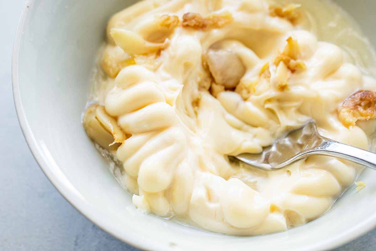 Creamy mayo with roast garlic cloves being mixed with a fork in a small bowl.