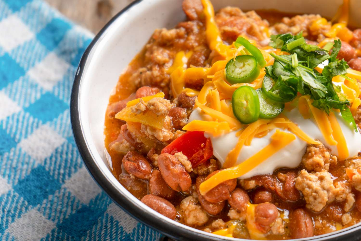 A bowl with a serving of chili, topped with sour cream, shredded cheese and sliced jalapeños