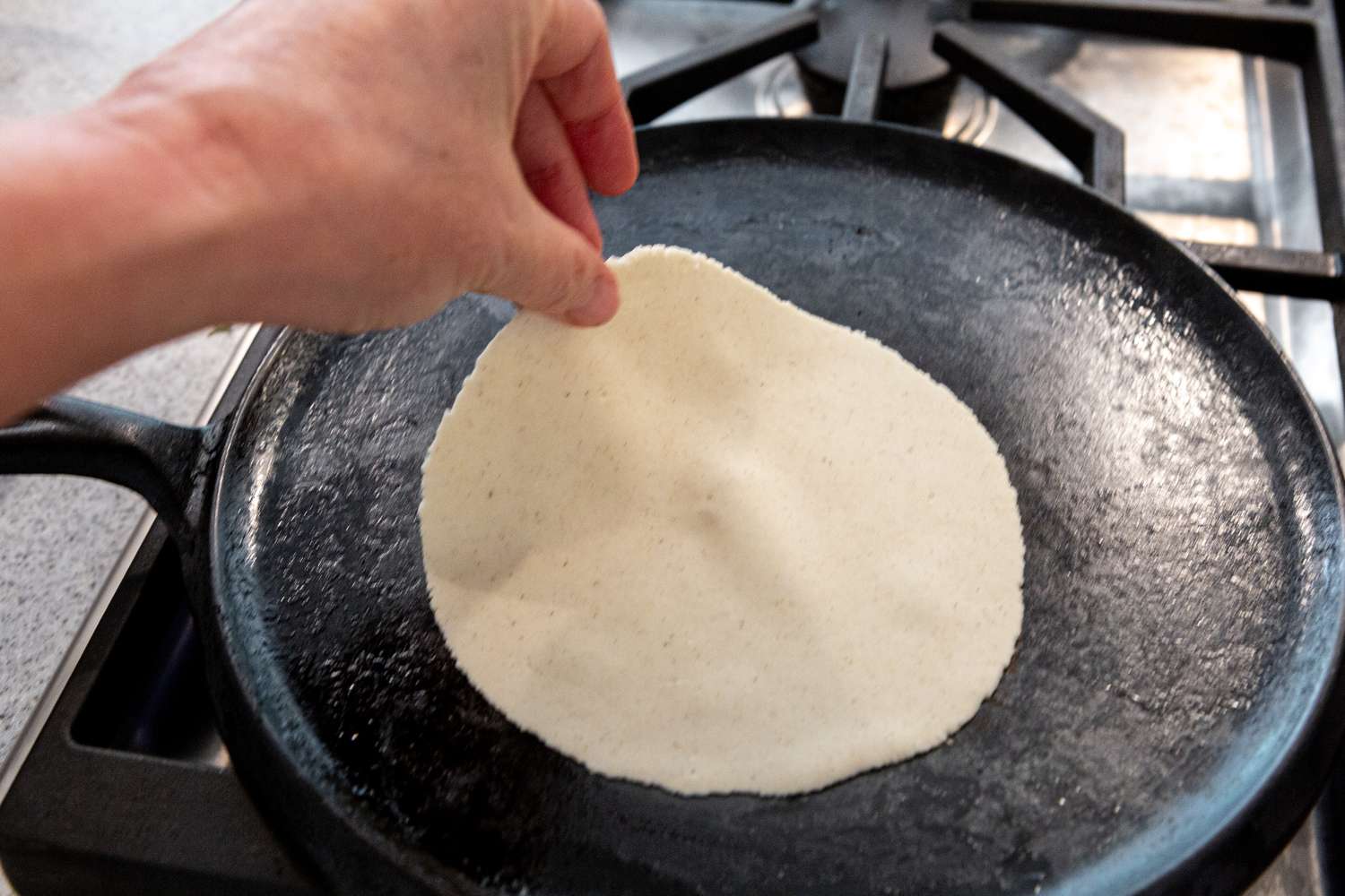 Laying a corn tortilla on a hot skillet