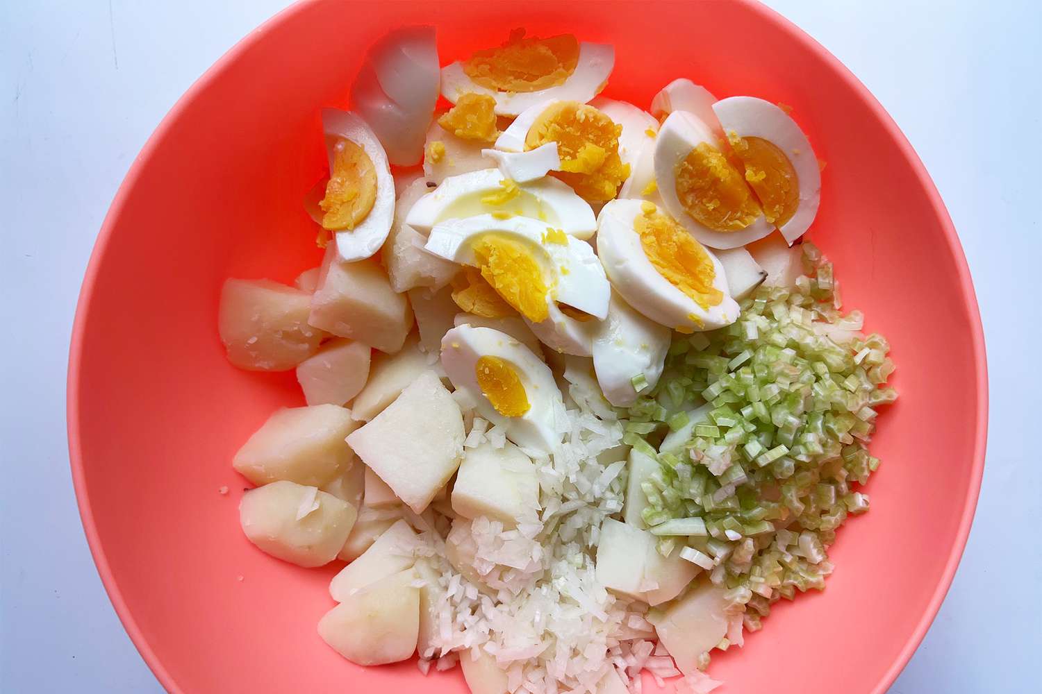 Potato salad ingredients in a bowl, including cooked potatoes, chopped eggs, celery, and onions