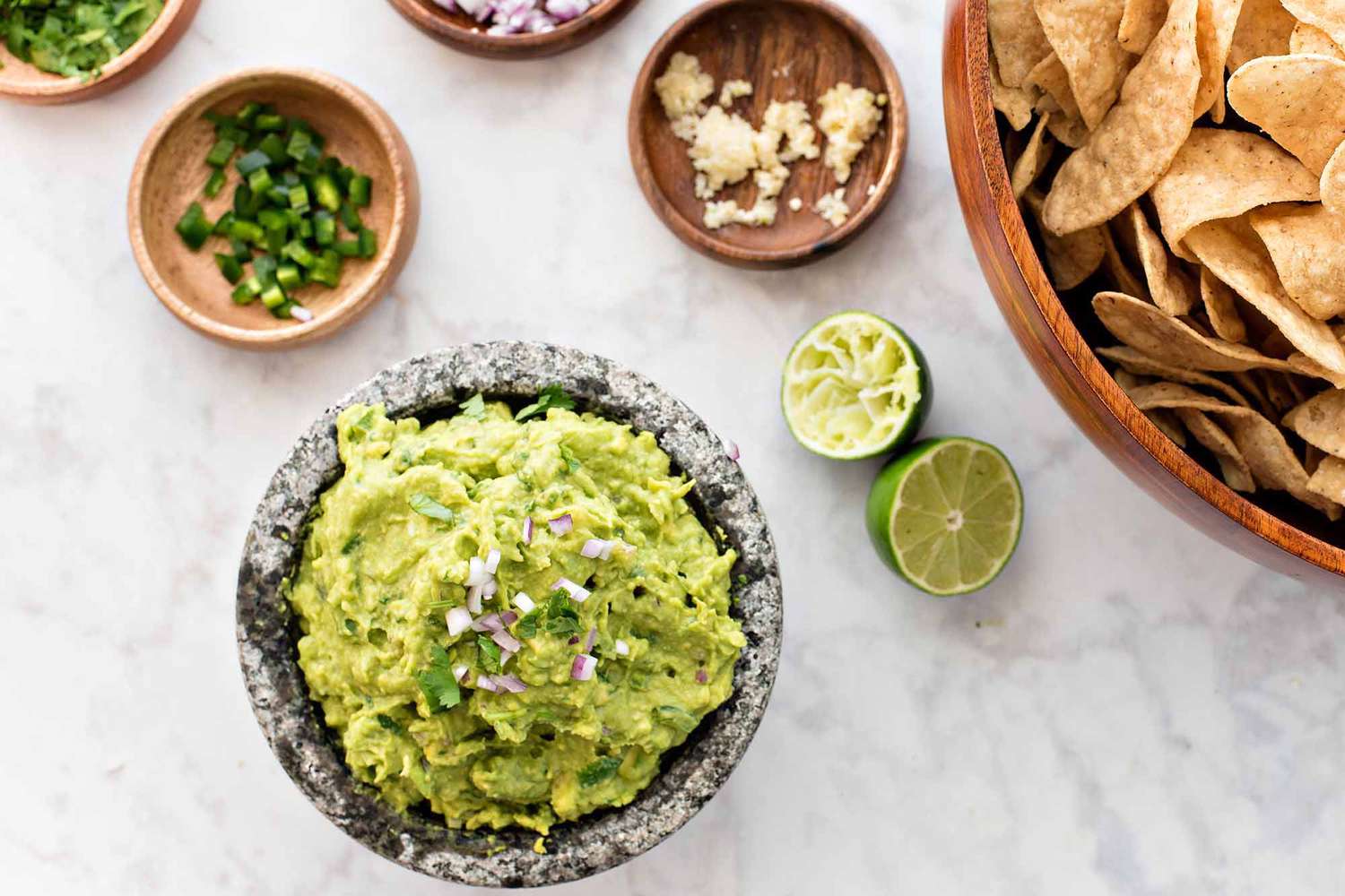 Guacamole with lime and cilantro - bowl of guacamole with smaller bowls of onion, cilantro, garlic and lime nearby and a big bowl of chips