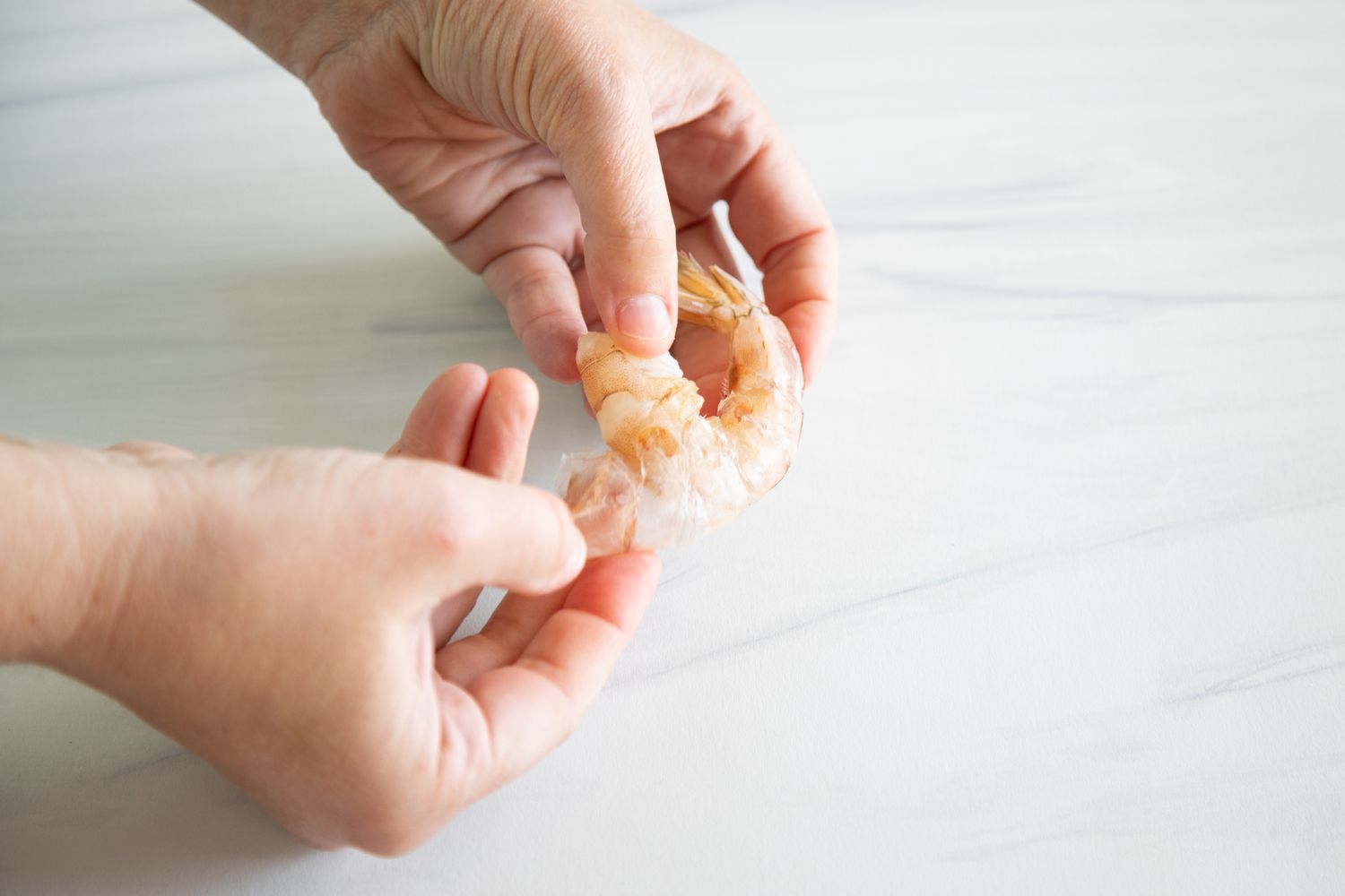 Hands showing how to devein shrimp.