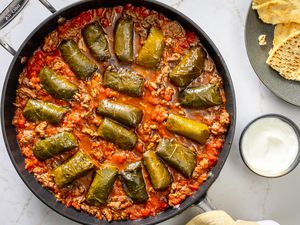 A skillet with dolmas cooked in tomato sauce and ground beef, served with pita bread and yogurt