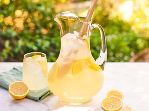 A pitcher and a glass filled with lemonade placed on a table, garnished with lemon slices