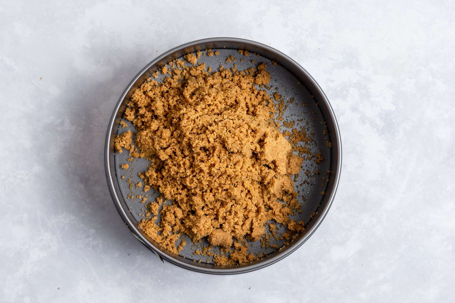 Graham cracker crust poured into a pan to make a no bake cheesecake recipe.