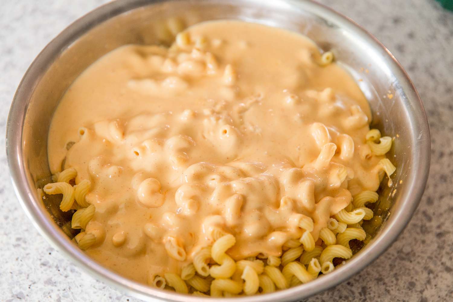 Angled view of a large metal bowl of pasta with the cheese sauce pored over it from Baked Mac and Cheese recipe