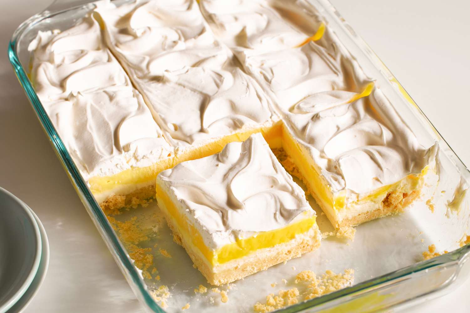 A tray of lemon dessert with a creamy topping and one piece removed