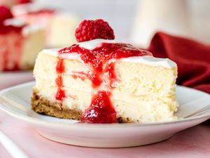 Side view of a slice of cheesecake topped with raspberry sauce.
