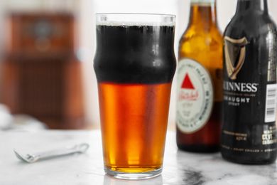 Glass of Black and Tan Next to Two Bottles of Beer and a Bottle Opener 