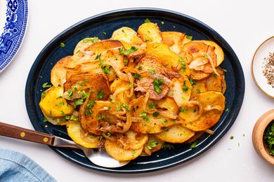 Lyonnaise potatoes on a platter at a tablet setting with a small plate of crushed peppers, bowl of minced parsley, and a plate 
