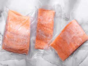 Three frozen salmon fillets in packaging on the counter