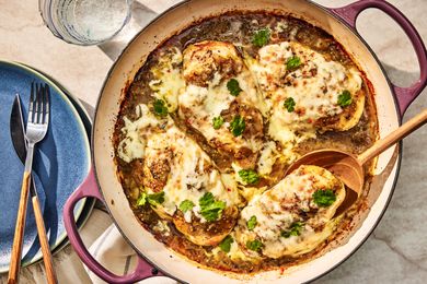 Overhead view of a skillet of Salsa Verde Chicken with a wooden serving spoon next to a plate with fork and knife and a drink glass