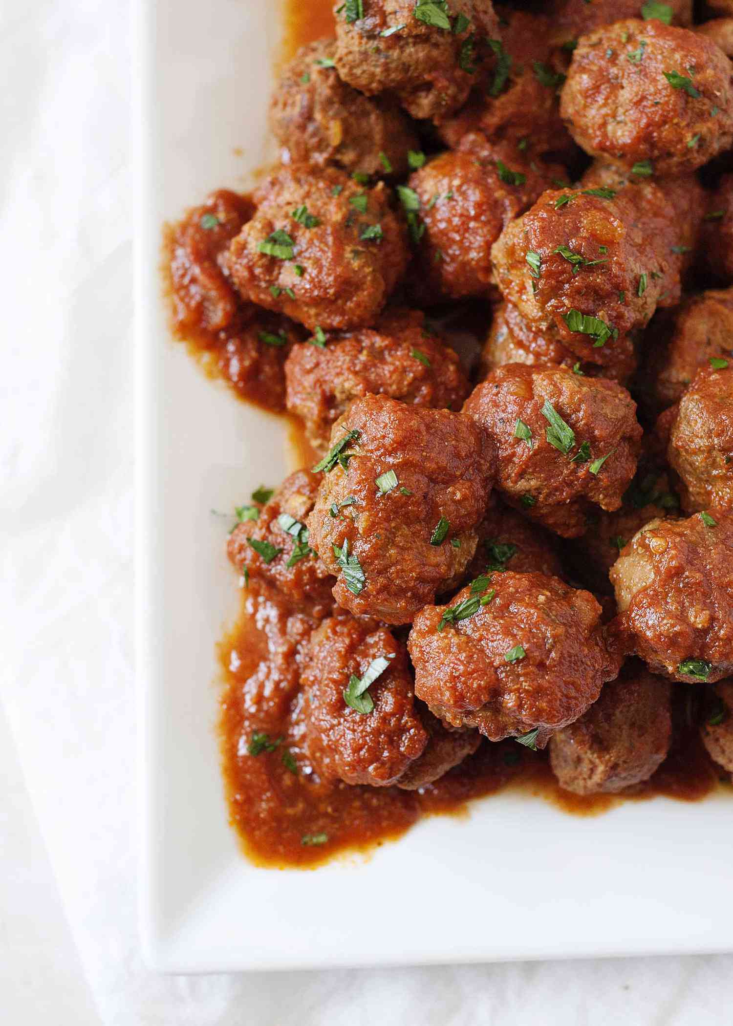 Best Slow cooker italian meatballs in tomato sauce piled onto a white serving platter with a spoon.