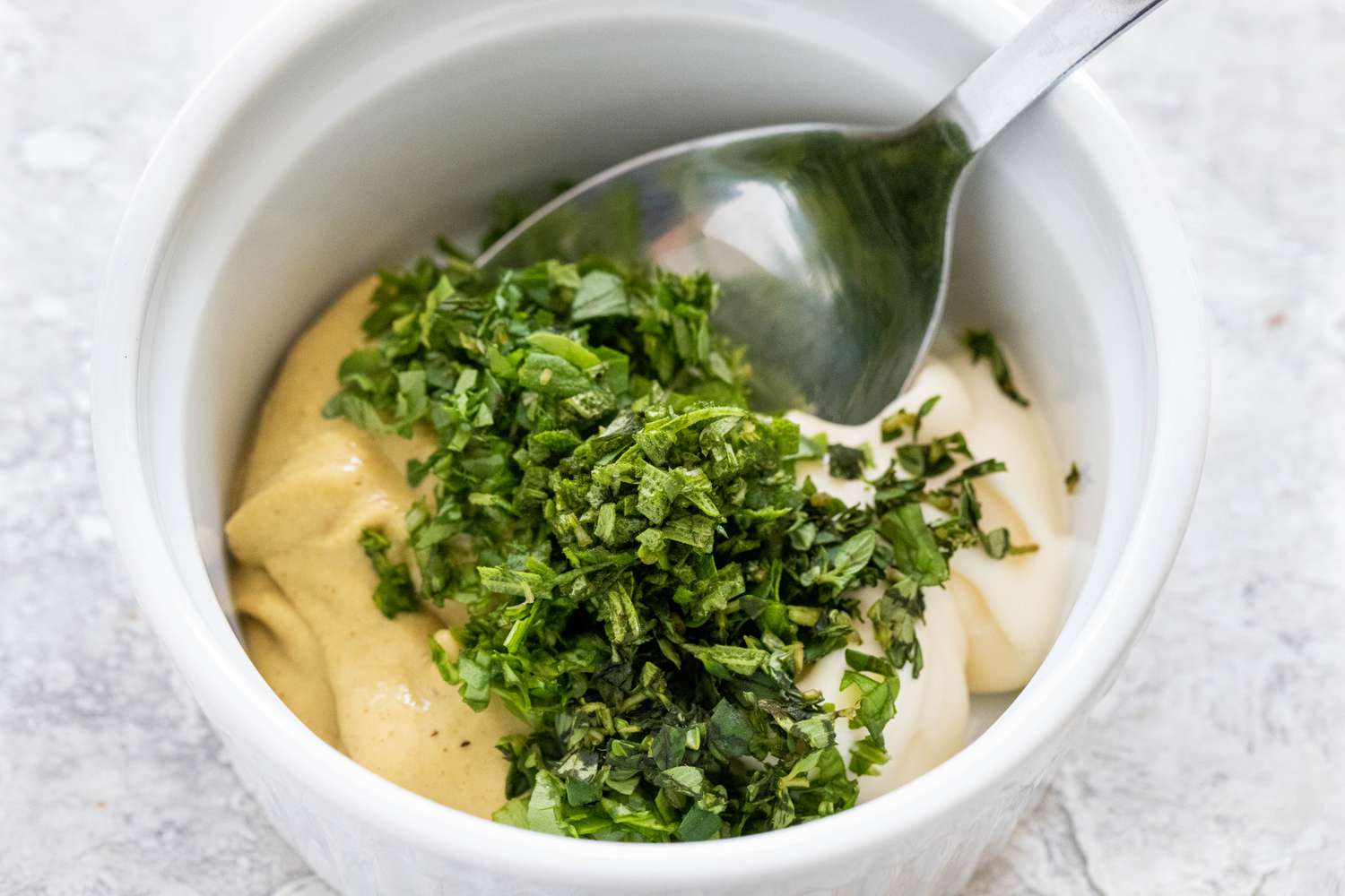 Mixing the herb spread for puff pastry pinwheels with prosciutto, Dijon mustard, and parmesan in a small bowl with a spoon.