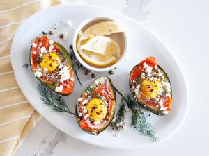 Overhead view of a platter of baked eggs in avocado and lemon slices.