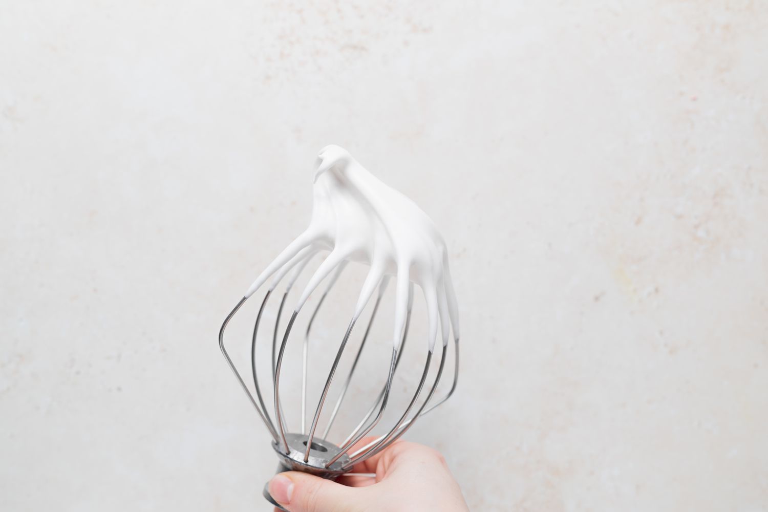 The whisk attachment with whipped mixture to make French macarons with peppermint white chocolate filling.