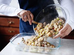 Woman in Blue Apron Spooning Stuffing from a Bowl to 9x13 Baking Dish 