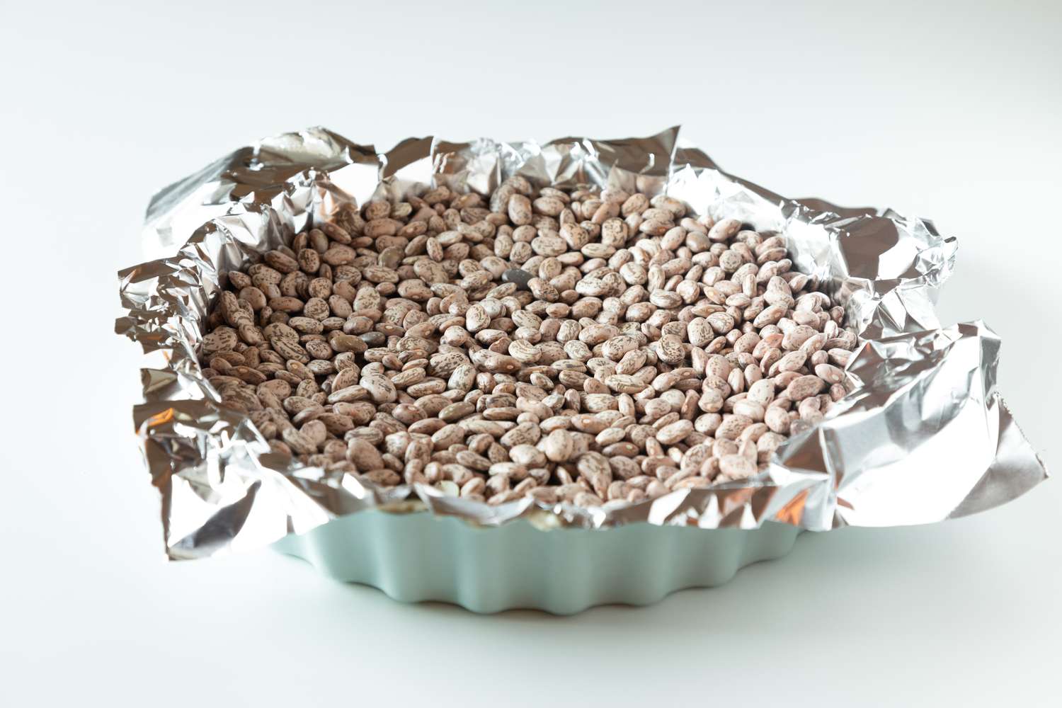 Foil and dried beans in a pan to make a quiche lorraine recipe.