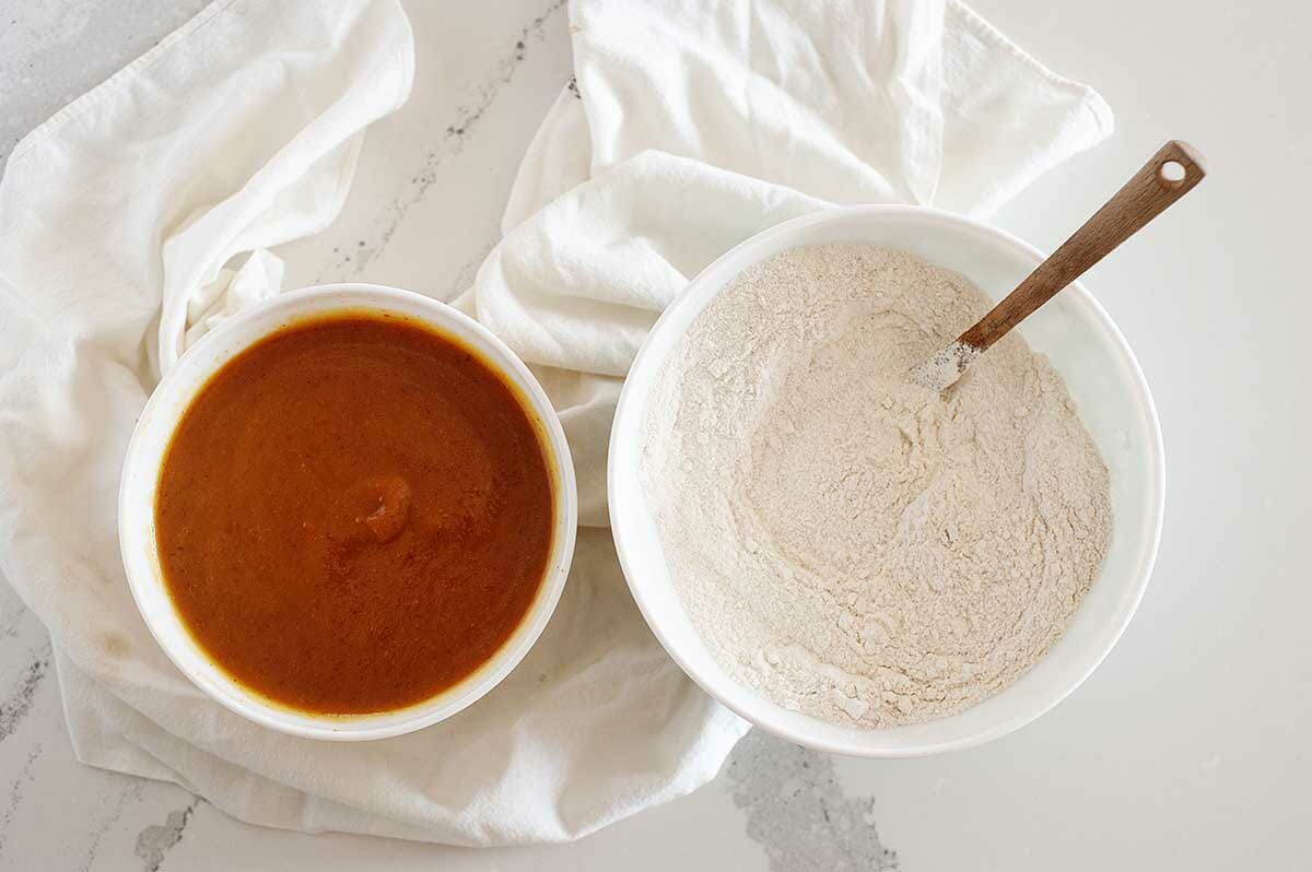 Flour mixture in a white bowl with pumpkin mixture in a second bowl to the left to show how to make Vegan Pumpkin Bread.