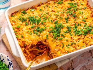 shipwreck casserole in a casserole dish at a table setting with a bowl of scallions, plate, and glass of water 