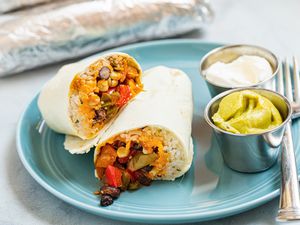 A plate of black bean, corn, and pepper freezer burritos with guacamole and sour cream on the side.