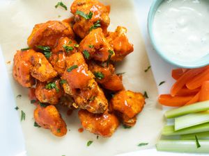 Air Fryer Buffalo Cauliflower Bites topped with sauce and next to a bowl of dip, carrots, and celery.