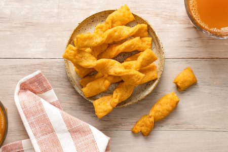 Twisted Cheese Straws on a Plate Next to a Drink and a Kitchen Towel. One Twisted Cheese Straw Is Broken in Half Next to the Plate.