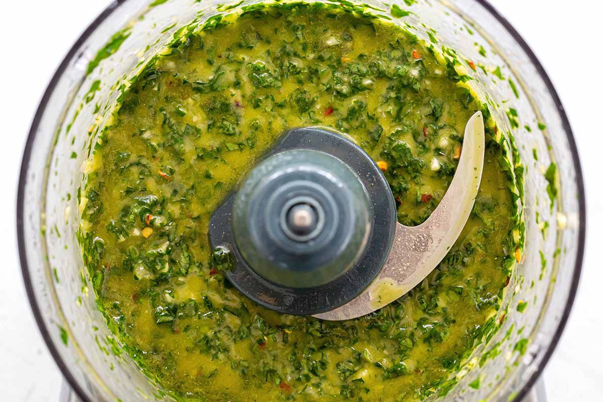 Herbs, spices and oils mixed together in a food processor to make chimichurri with avocados