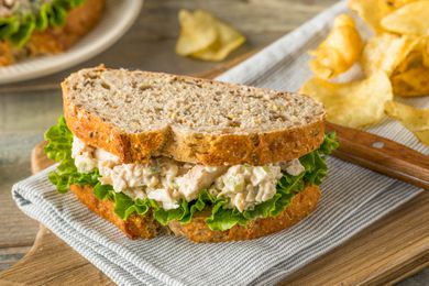 chicken salad and chips on a table napkin over a wooden board 