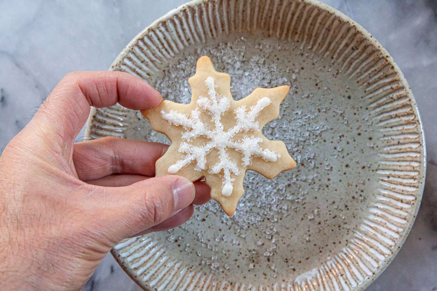 Sparkling sugar added to the top of a snowflake cookie decorate using an Easy Royal Icing Recipe.