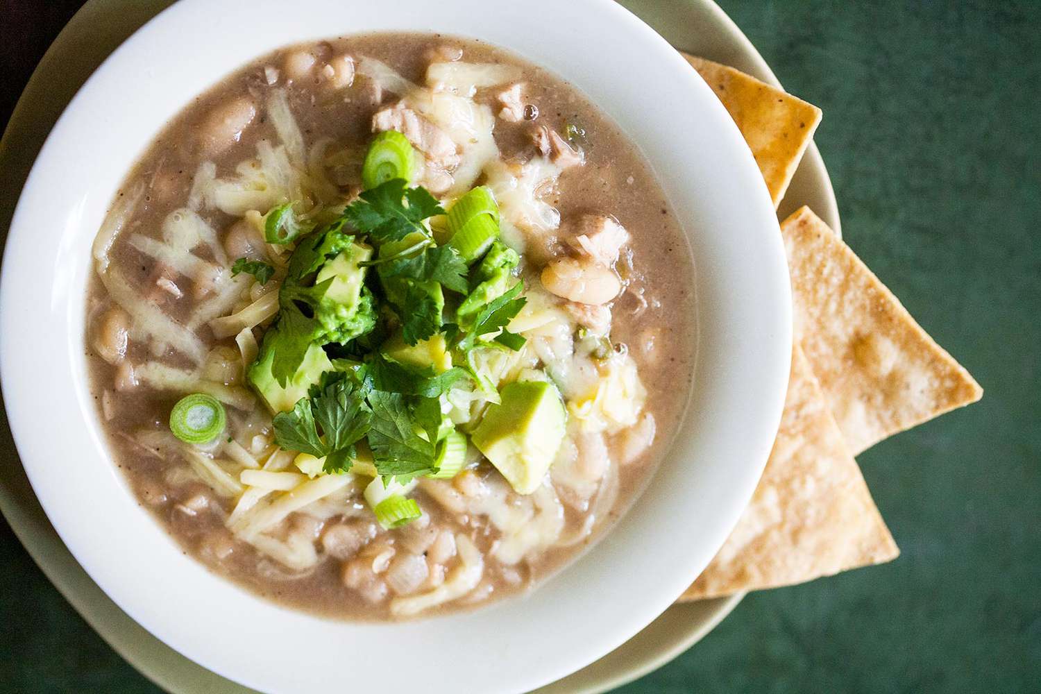 white turkey chili topped with cheese and cilantro in a white bowl with tortilla chips on the side