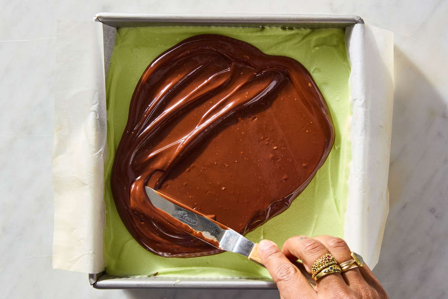 overhead view of hand with knife spreading ganache on top of mint mixture for Mint Brownies