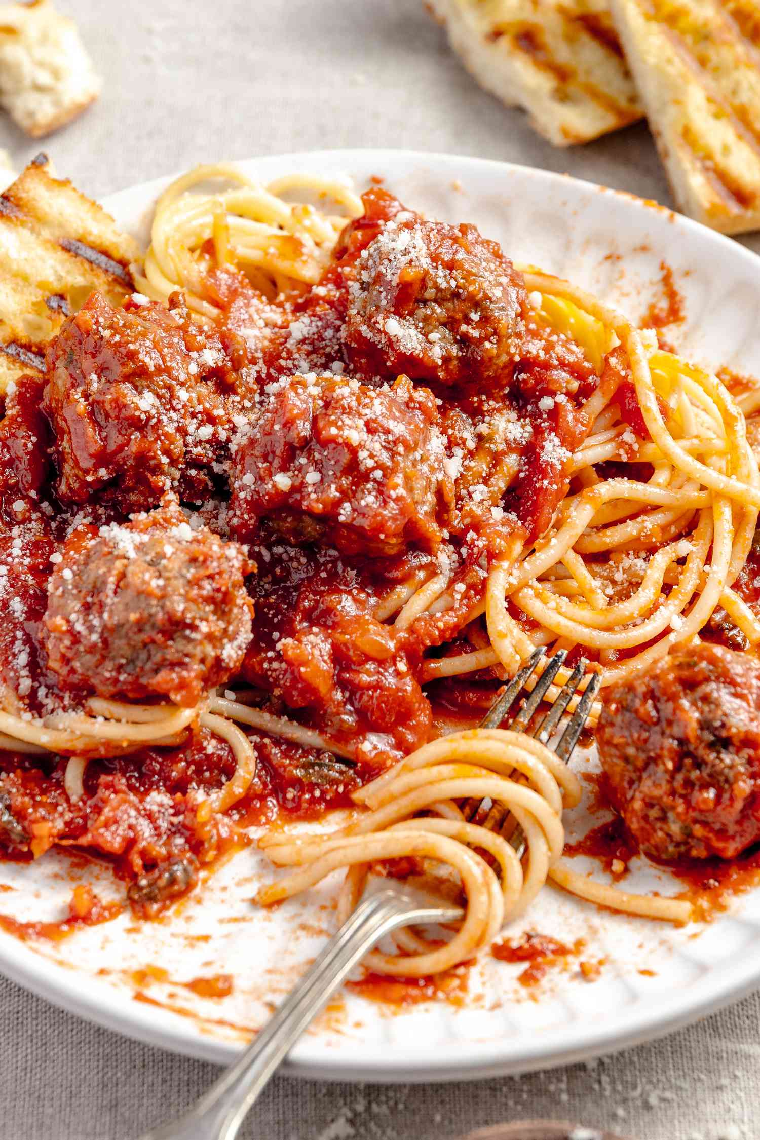 Plate of Spaghetti and Meatballs and a Slice of Toasted Bread. Some of the Spaghetti Is Wrapped Around a Fork Sitting on the Plate. In the Surroundings. More Toasted Bread. 