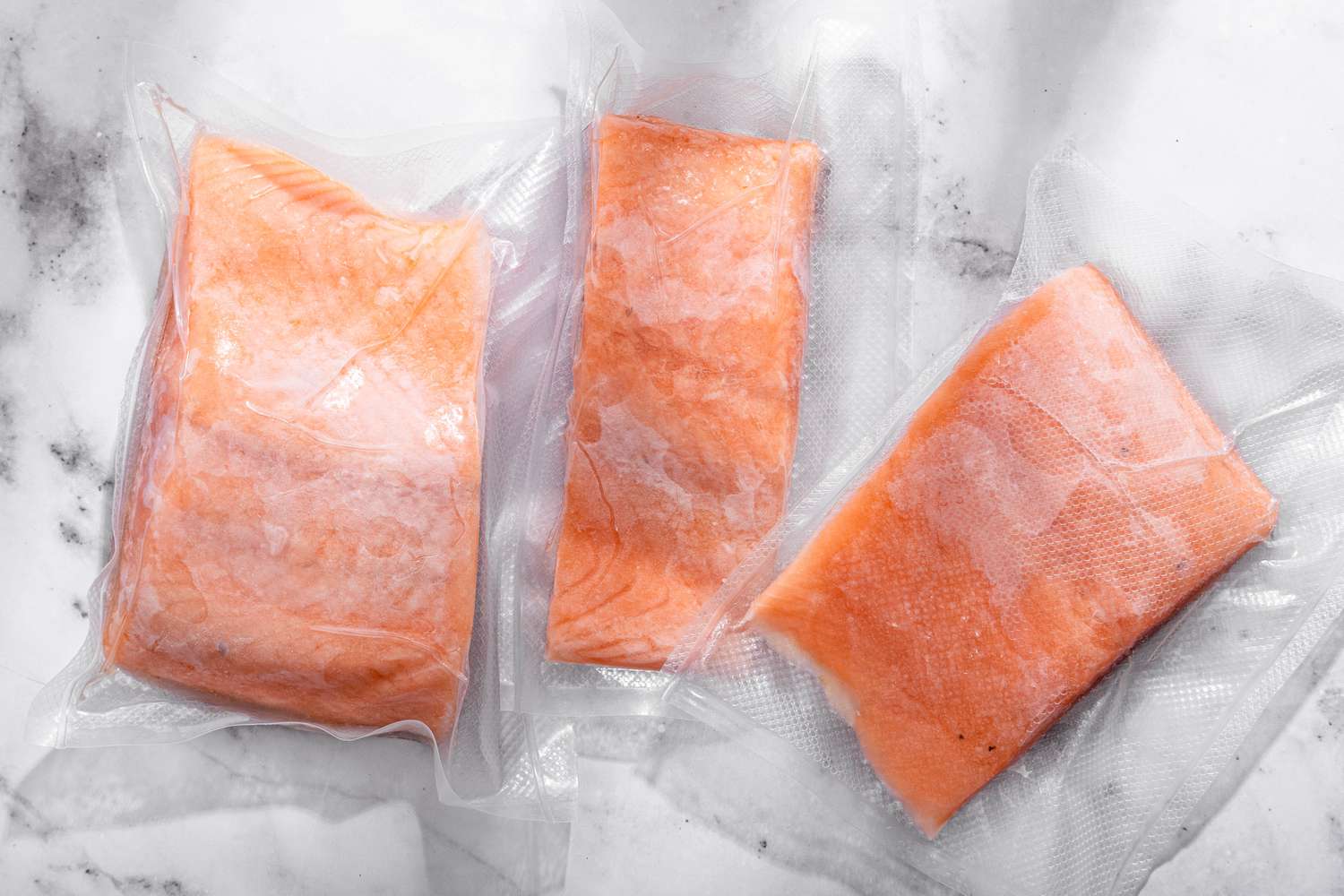 Three frozen salmon fillets in packaging on the counter