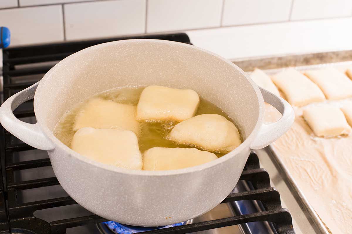 A dutch oven is on a stove and has five homemade beignets frying in oil.