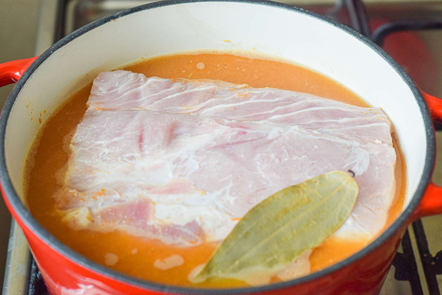 A dutch oven with pork shoulder roast set inside with sauce to make how to make pulled pork.