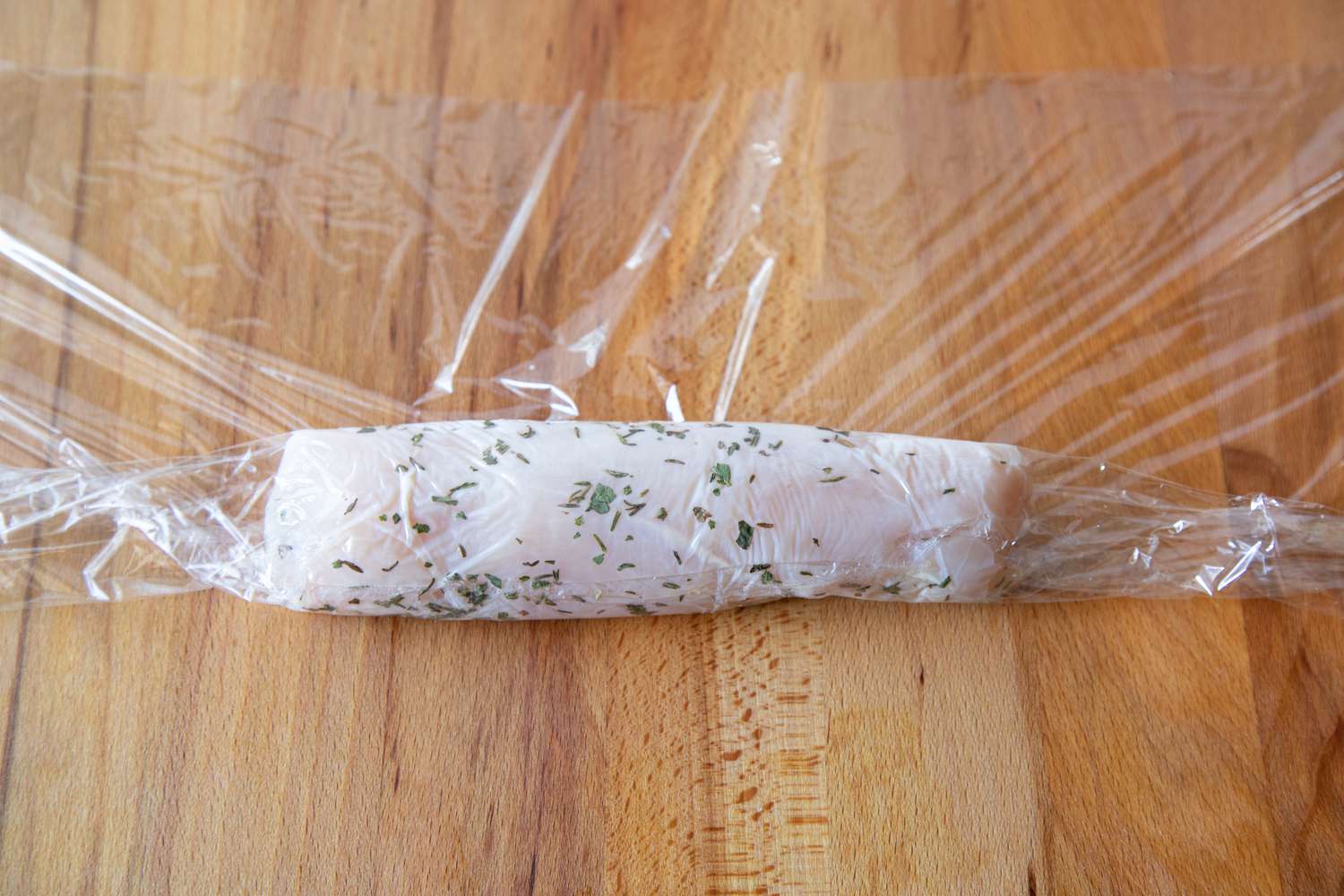 Wrapping marinated chicken in plastic wrap to make a poached chicken recipe.