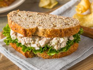 Chicken salad sandwich on whole-grain bread, with lettuce and potato chips in the background.