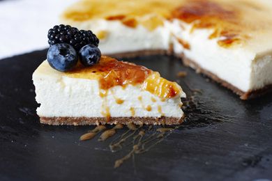 Vanilla Bean Cheesecake with brittle sugar topping on a slate board wtih a slice cut out and fruit nearby.