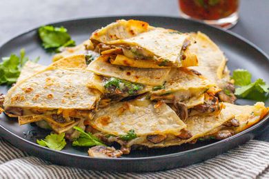 Vegetarian Quesadilla Recipe -close up of cheese and mushroom quesadillas stacked on top of each other with a jar of red salsa in the background.