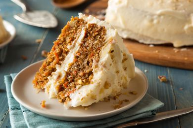 Sideview of a two layer carrot cake slice in the foreground with the rest of teh cake in the background