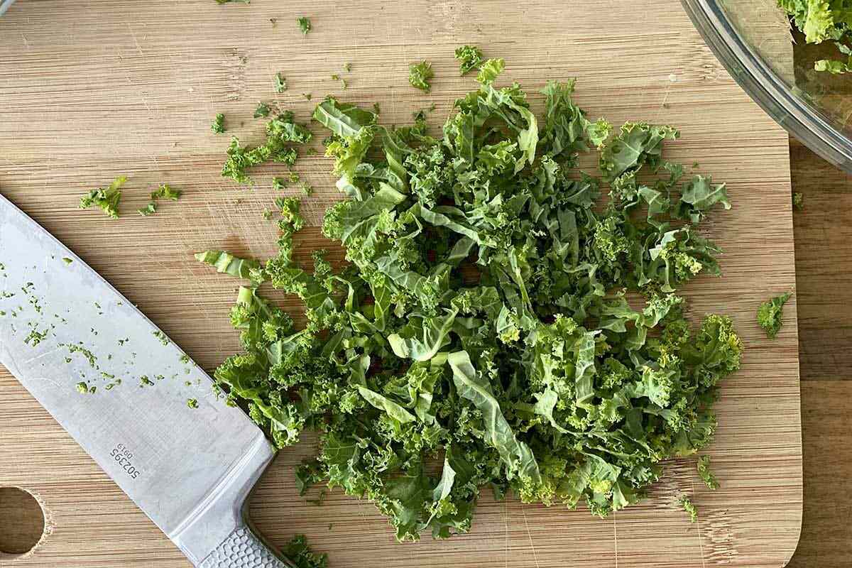Kale being chopped on a cutting board for a Fall Vegetable Salad with Bacon and Maple Dijon Vinaigrette.