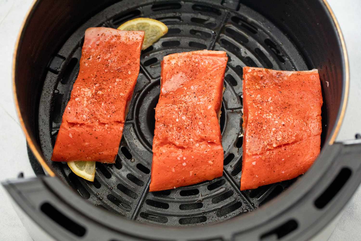 Raw Salmon Fillets Added to Air Fryer on Top of Lemon Slices