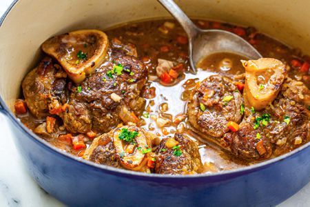Ladling osso buco out of a dutch oven.
