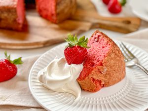 Slice of strawberry cake with whipped cream and a whole strawberry on a plate