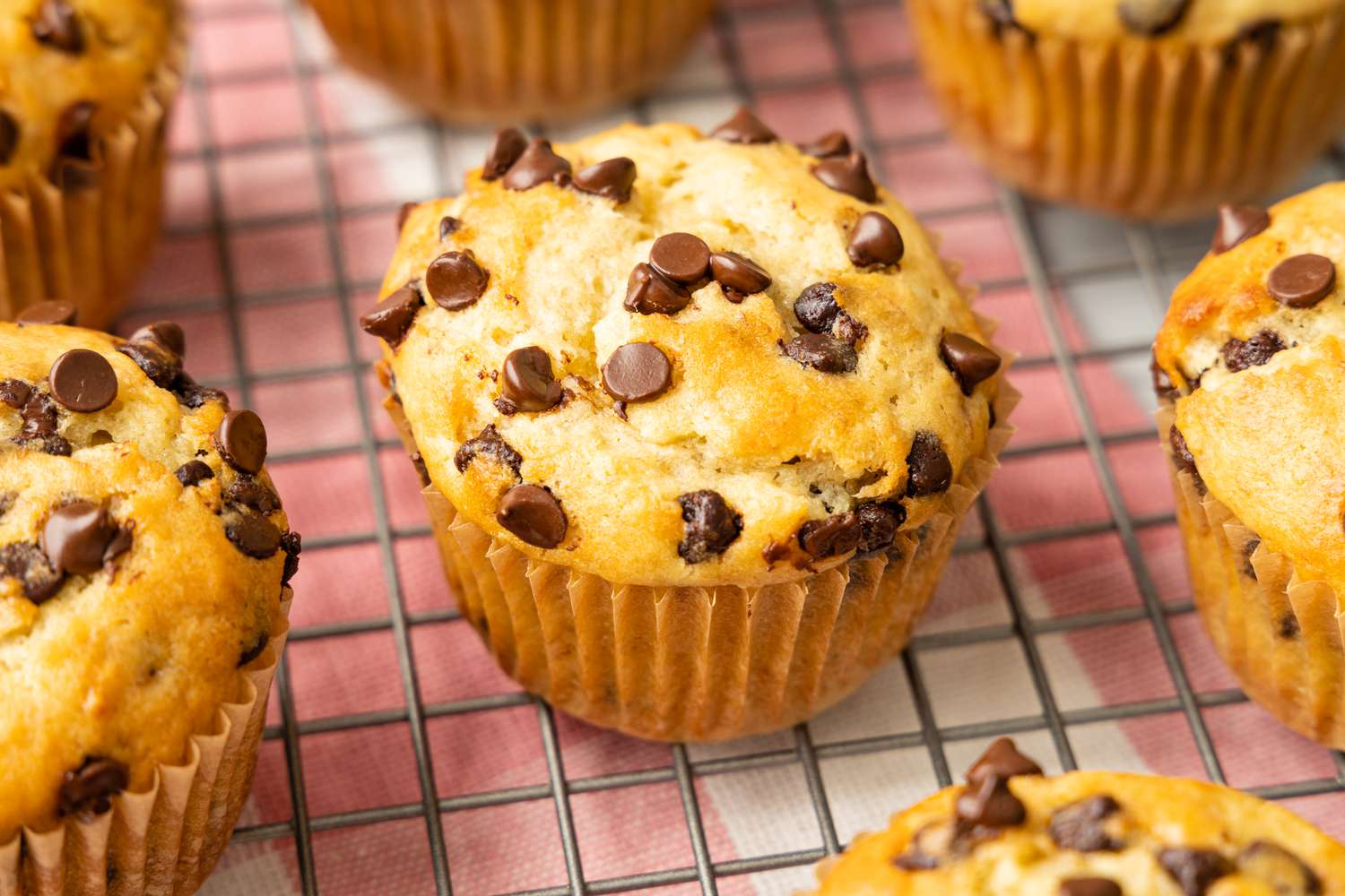 Banana Chocolate Chip Muffins on a Cooling Rack Over a Red and White Checkered Kitchen Towel